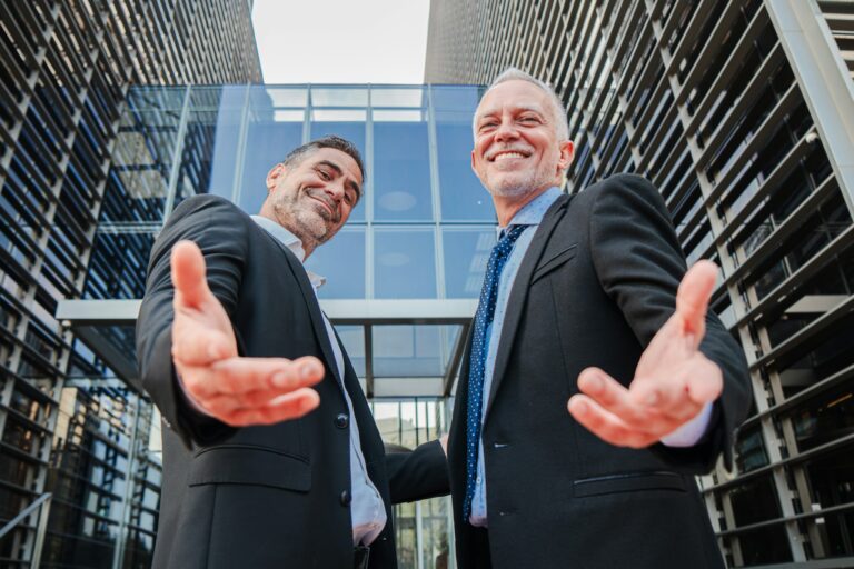 Confident businessmen in suits extending their arms for a warm greeting, standing outside a modern